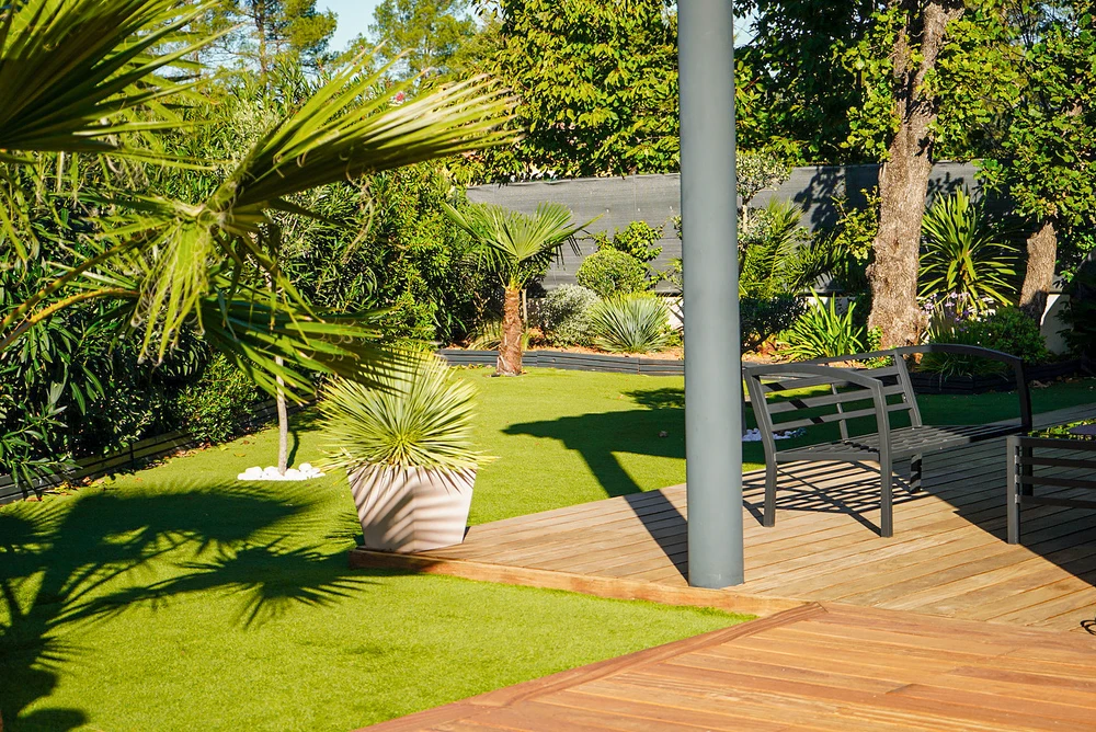 Jardin paysager contemporain extérieur, terrasse en bois composite avec banc métal anthracite et poteau central