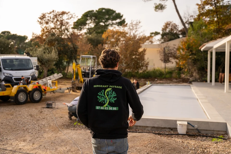 Sc&egrave;ne ext&eacute;rieure de jardinage, personne en pull bordeaux tenant d&eacute;licatement un plant avec motte de terre et mousse entre ses mains au-dessus d'un bac de plantation en bois