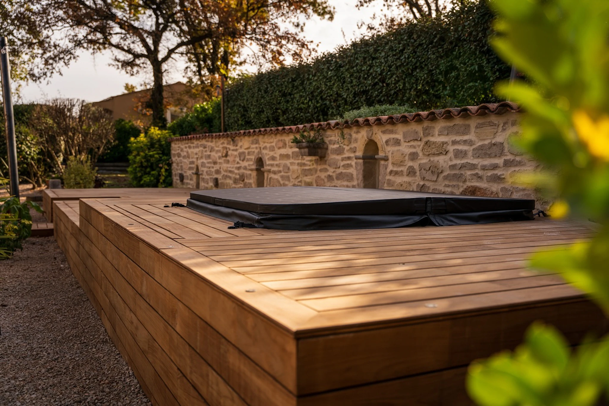 Terrasse extérieure en bois avec garde-corps à barreaux verticaux donnant sur jardin verdoyant et forêt dense d'arbres feuillus