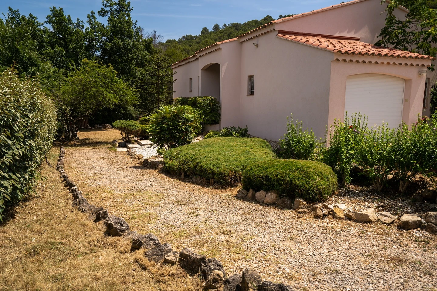 Jardinier professionnel en combinaison bleue taille une haie dense avec un taille-haie électrique à perche télescopique dans un espace vert résidentiel